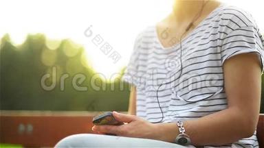 在公园里，一个带着耳机听着智能手机音乐的女人，一个使用智能手机的漂亮女人